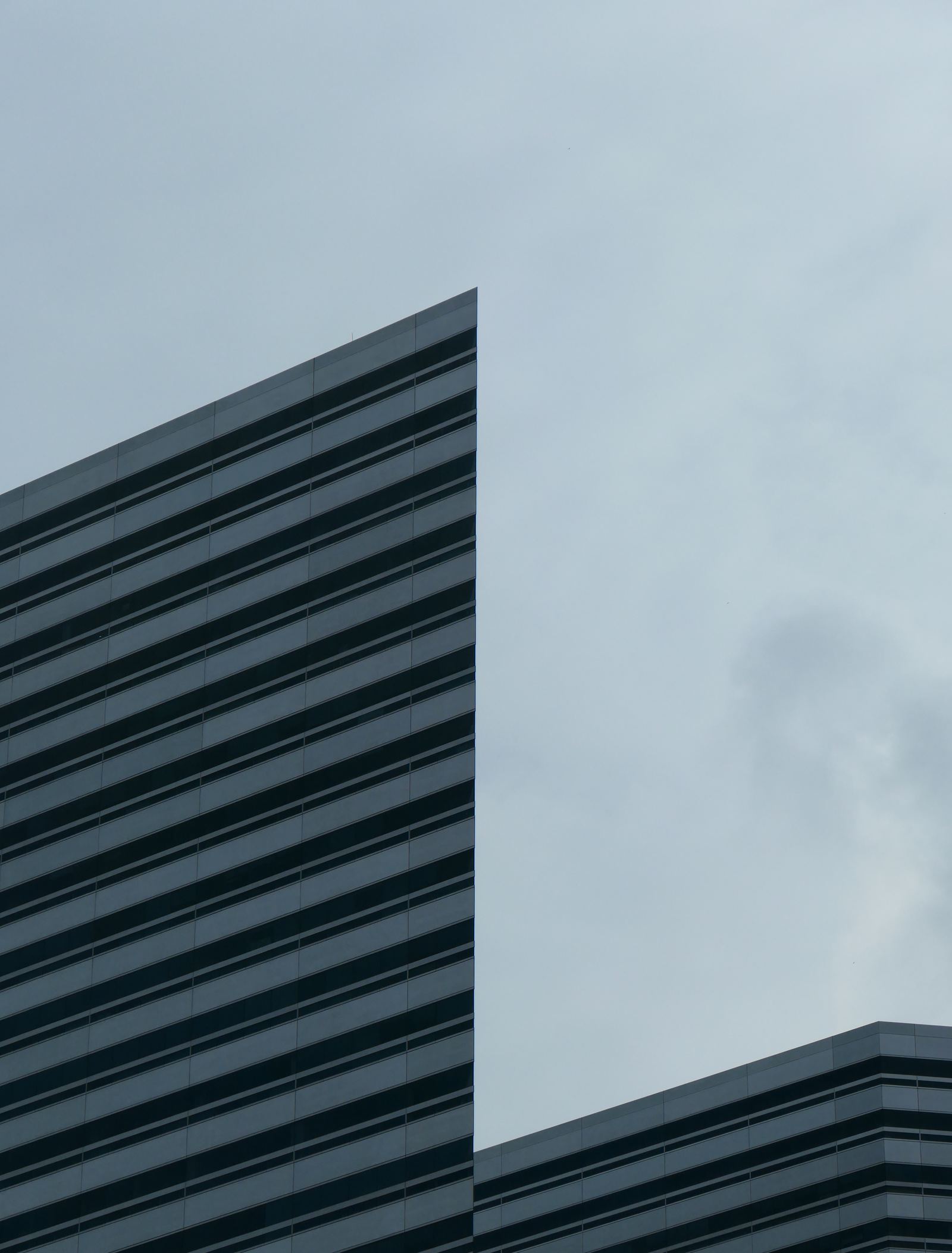 Angle d'un immeuble de bureaux à bandeaux horizontaux se détachant sur un ciel couvert
